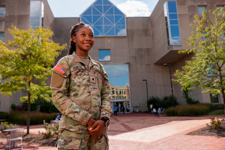 A female soldier stands in front of the University Library.