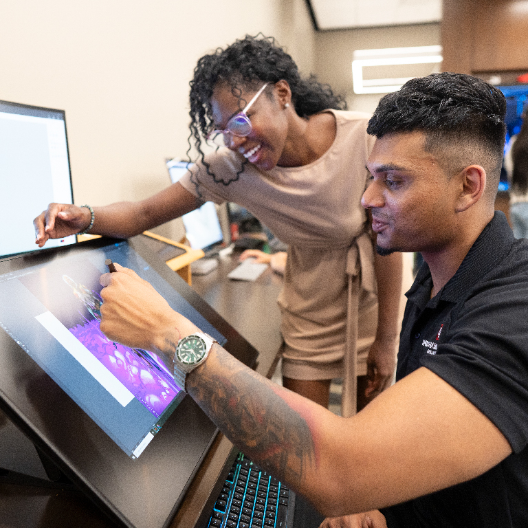 A professor assisting a student with a project on a large drawing tablet